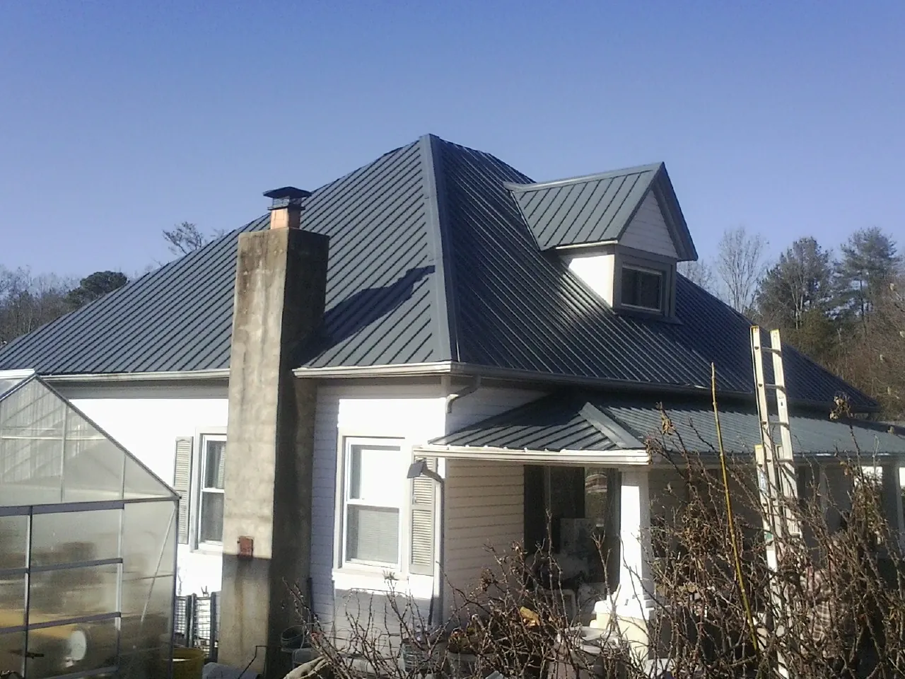 Dark blue standing seam metal roof on a white farmhouse with dormer — Slate & Tile Roof Repair by Roofing Brothers in Ridgway