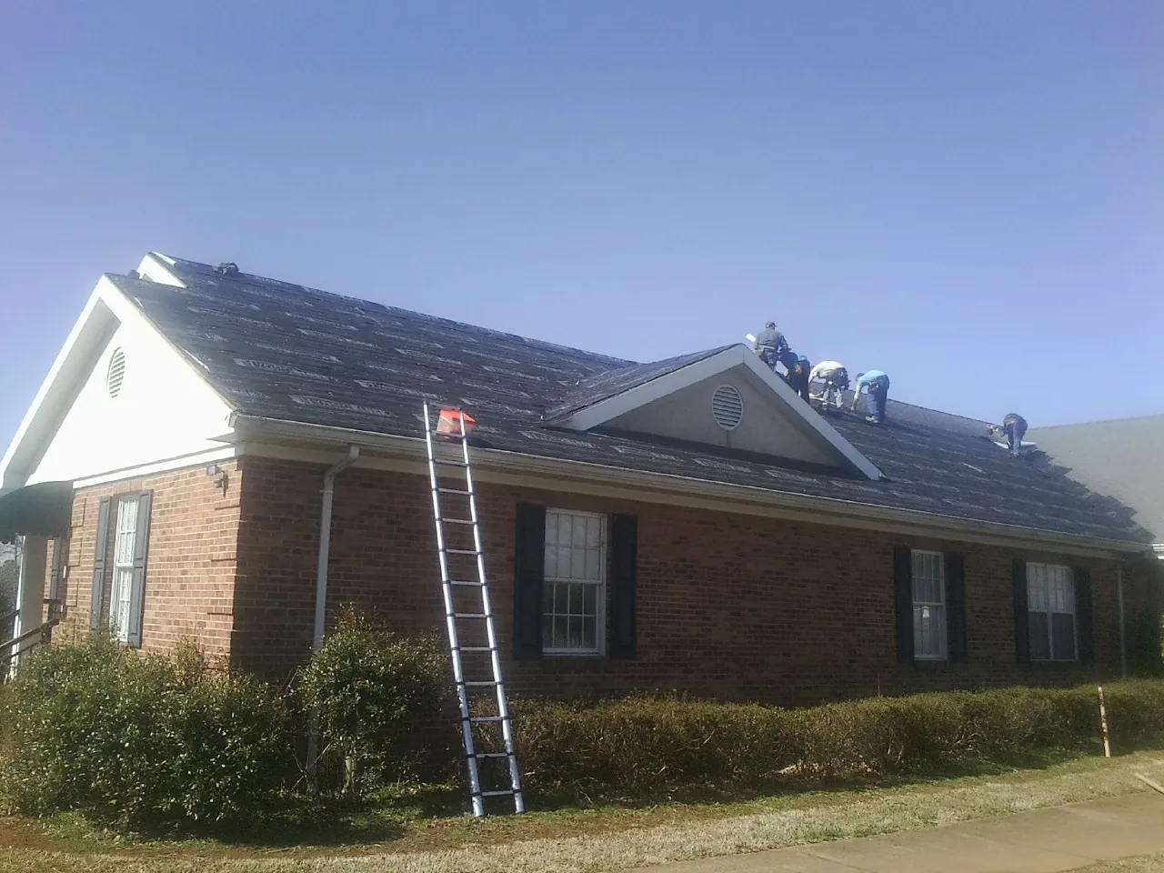 Crew tearing shingles off a brick ranch roof with a ladder set — Emergency Roof Repair work by our crew in Ridgway