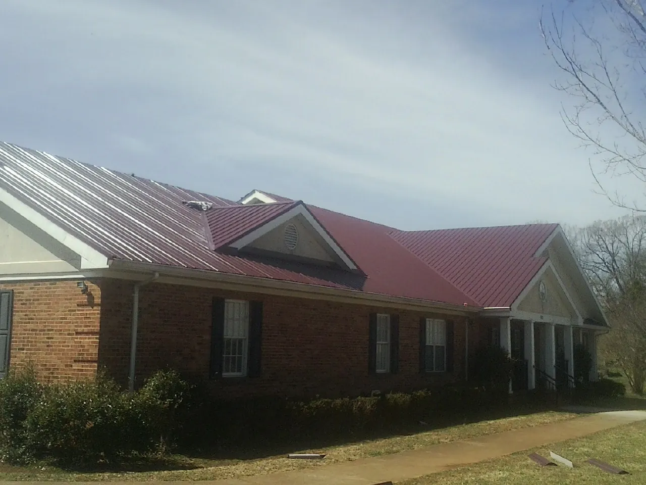 Red metal roof with gabled entries on a long brick building, from a Hail Damage Roof Repair job in Ridgway