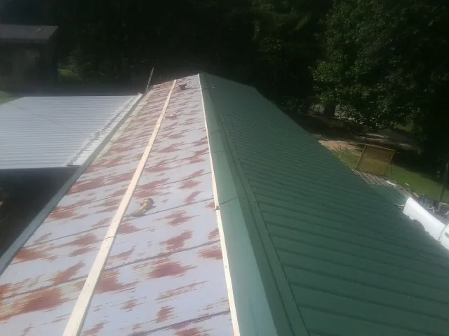 Old rusted panels beside newly installed green metal roofing — Wind Damage Roof Repair by Roofing Brothers in Ridgway