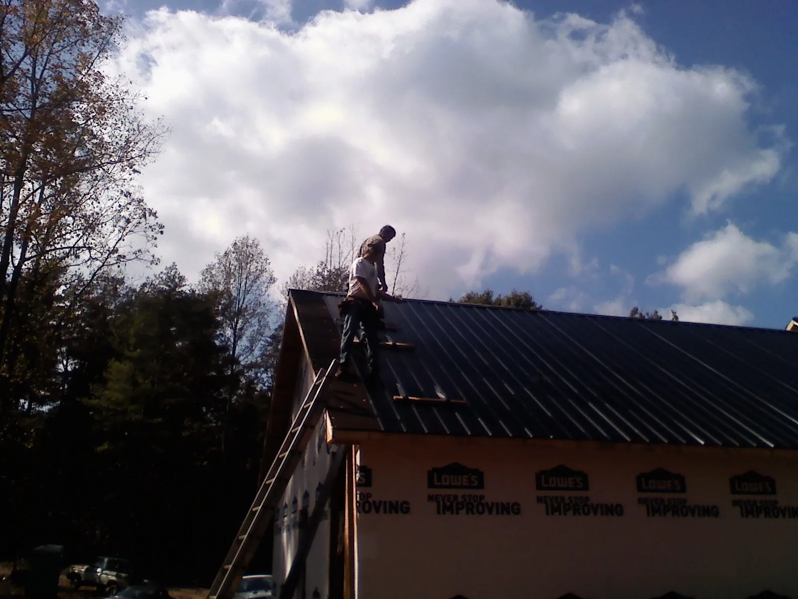 Roofer fastening dark metal panels high against a cloudy sky, from a Roof Inspection job in Ridgway